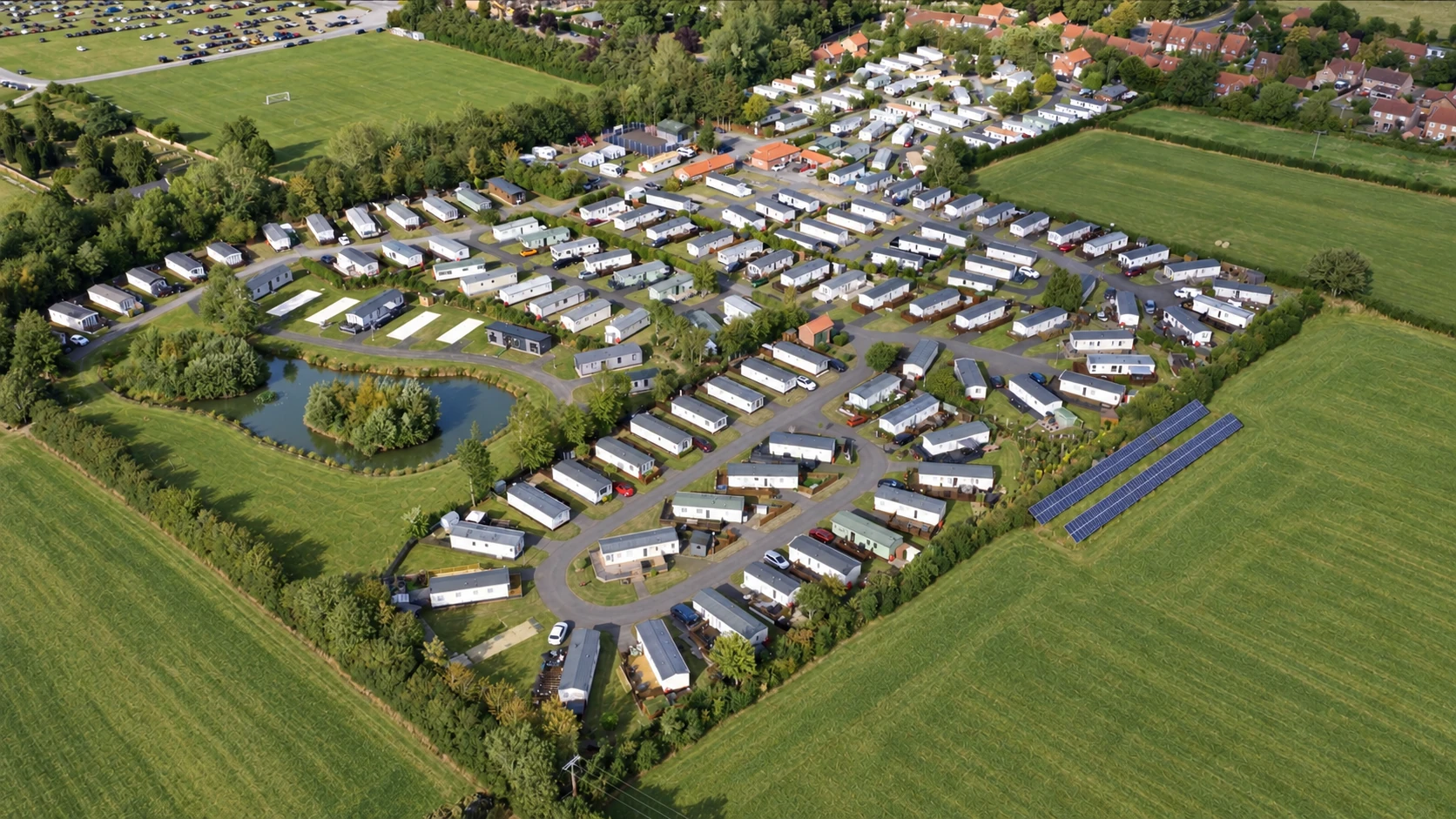 Aerial view across Ashfield Caravan Park showing holiday homes, the lake, surrounding fields and solar panels